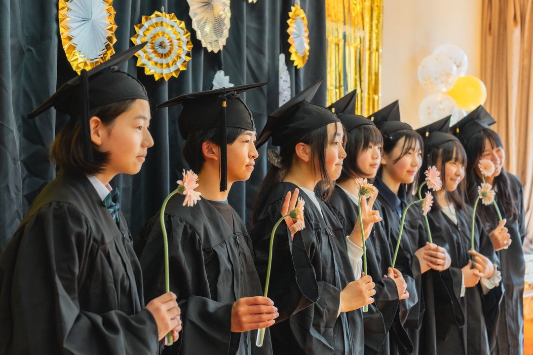 ISN graduates in caps and gowns standing in a row at the graduation ceremony, each holding a gerbera flower
