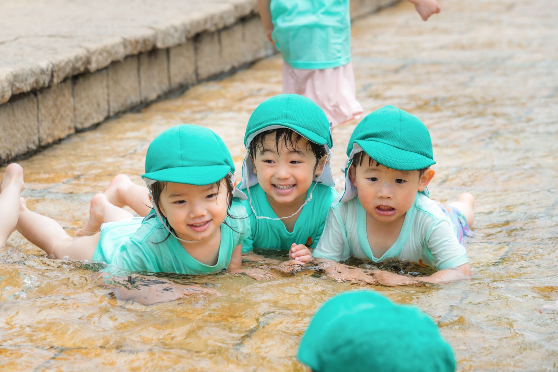 ISN children lying side by side in shallow water, smiling at the camera
